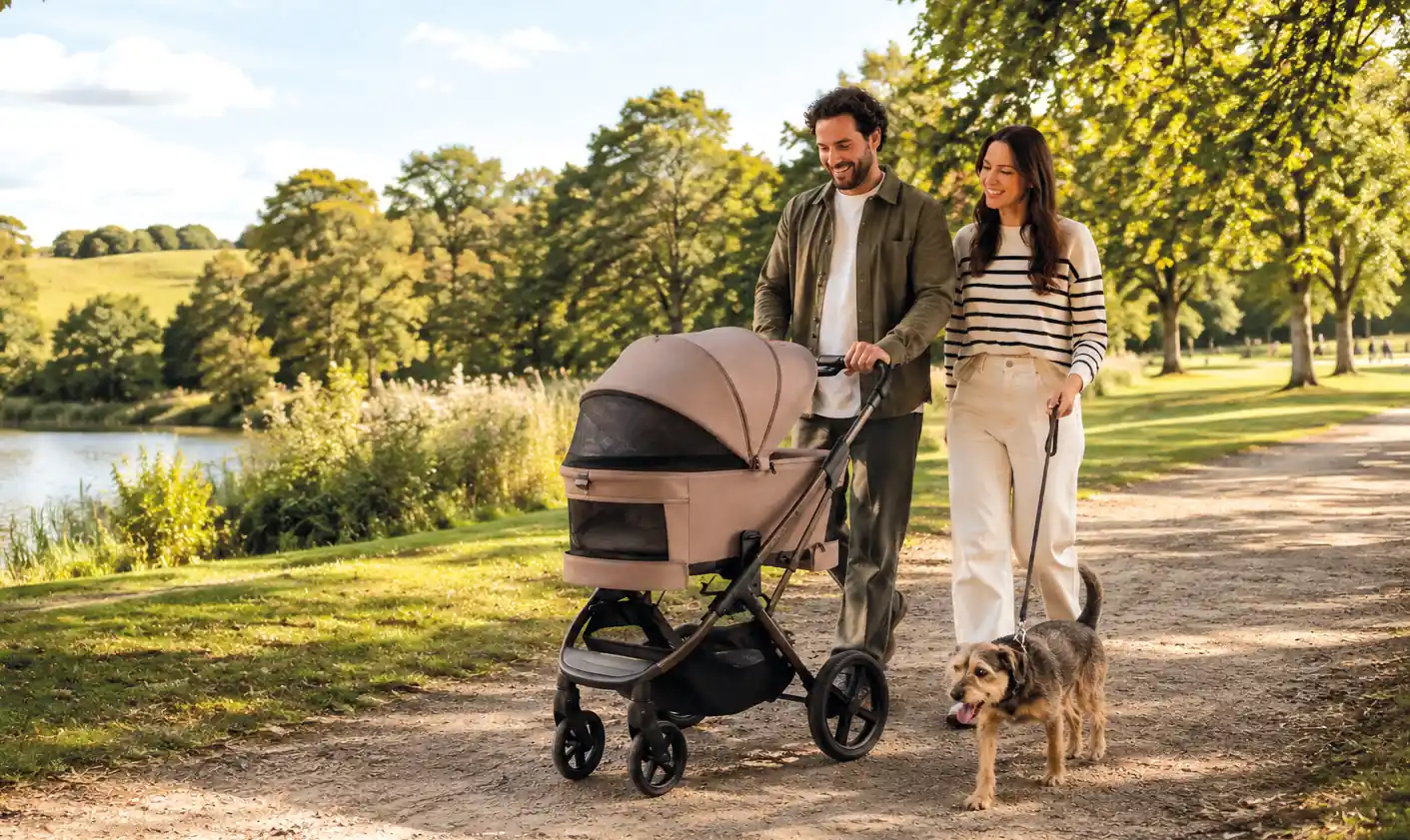 Eltern spazieren mit dem MOON CIAO Fold Kinderwagen und Hund durch einen Park am See